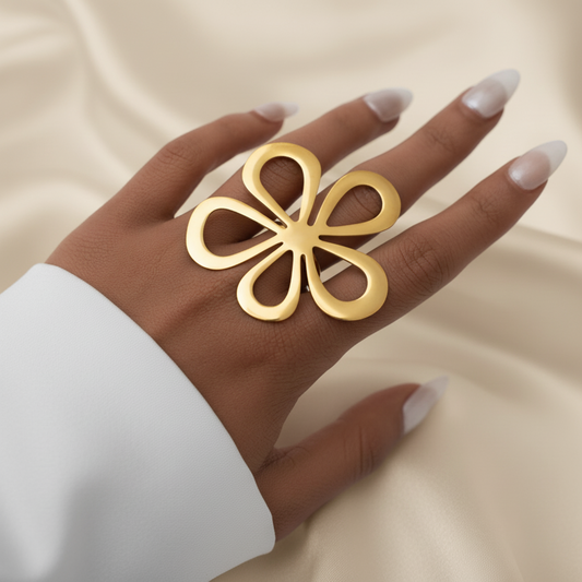 Main de femme portant une bague ajustable en acier inoxydable doré avec grande fleur stylisée ajourée.