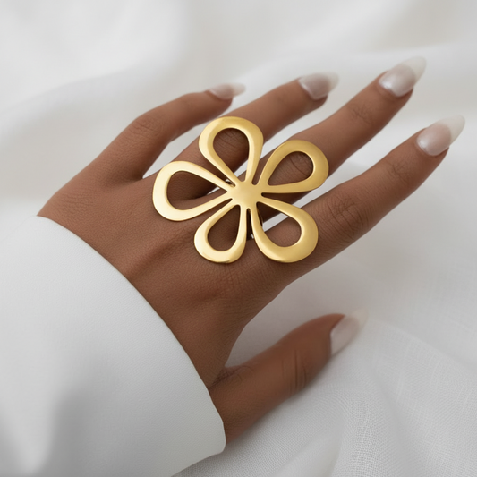 Main de femme portant une bague ajustable en acier inoxydable doré avec grande fleur stylisée ajourée.