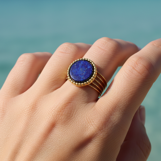 Main de femme portant une bague dorée en acier inoxydable ornée d'une pierre naturelle lapis-lazuli.