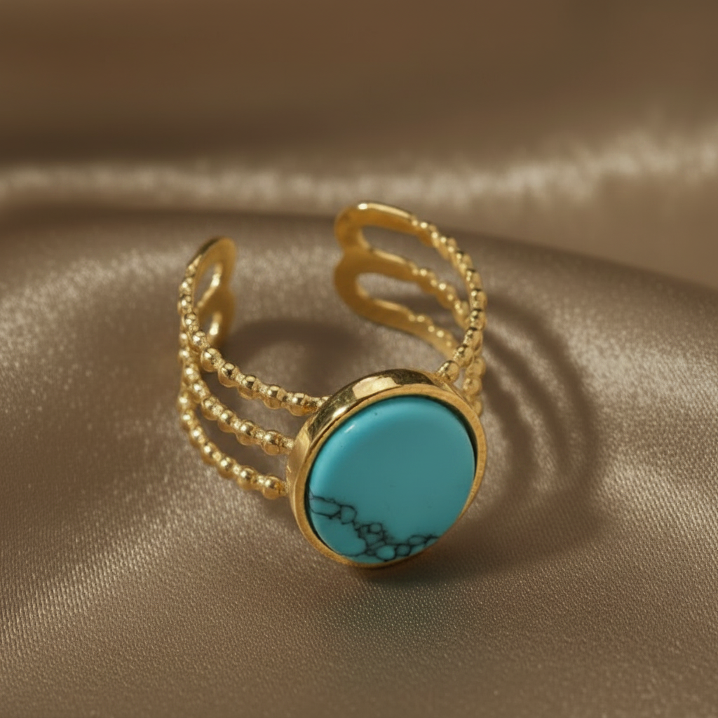 Gros plan sur une bague dorée en acier inoxydable ornée d'une pierre naturelle turquoise.