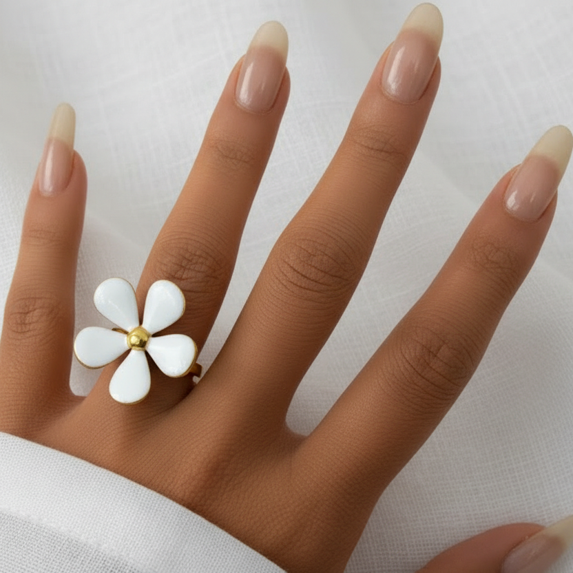 Main de femme portant une bague fleur en acier doré et émail blanc.