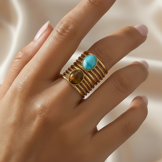 Bagues dorées en acier inoxydable et pierre naturelle turquoise et oeil de tigre portées sur une main de femme.