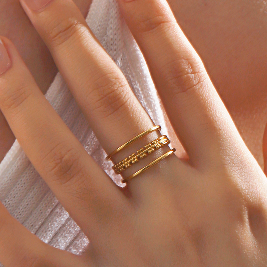 Bague dorée ajustable en acier inoxydable composée de deux anneaux et d’un motif de petites fleurs ajourées portée sur la main d’une femme