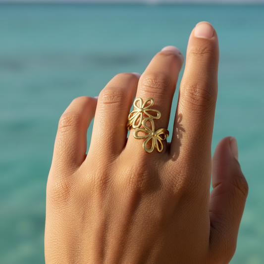 Main de femme portant une bague dorée en acier inoxydable ajustable ornée de deux fleurs ajourées.