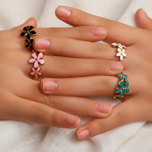 Mains portant des bagues ajustables en acier inoxydable doré ornées de trois fleurs en émail, disponible en bleu, rose, noir et blanc