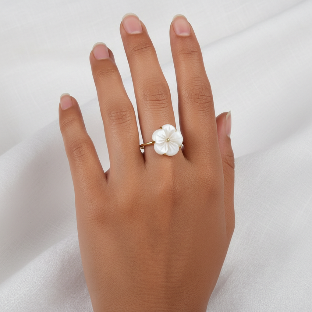 Main de femme portant une bague dorée en acier inoxydable ornée d’une fleur en nacre.