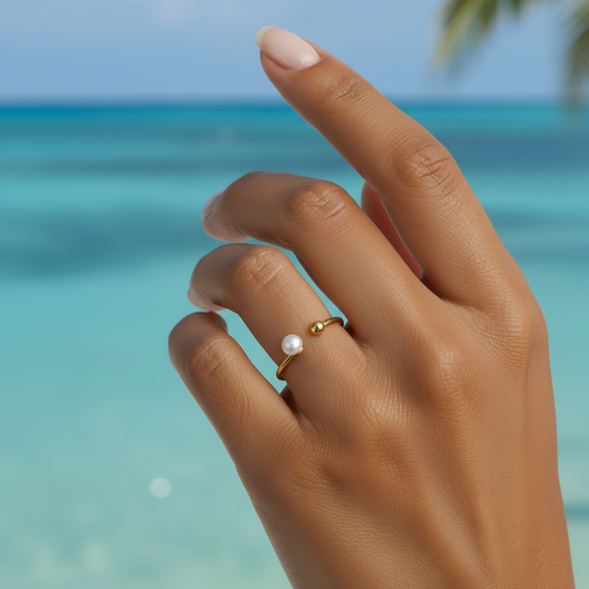 Main de femme portant une bague dorée en acier inoxydable ornée d'une perle d'eau douce naturelle.