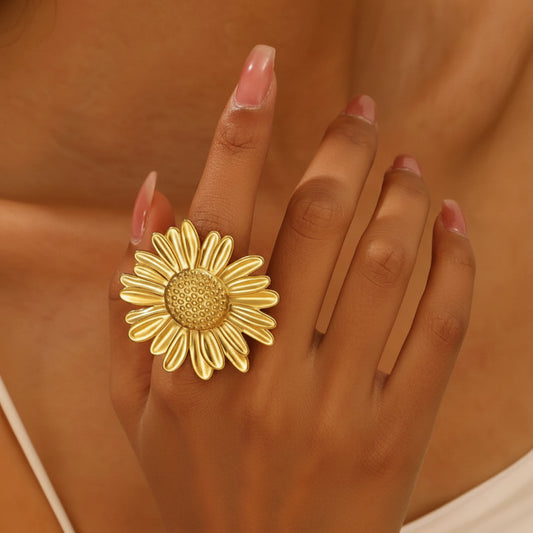 Main portant une bague dorée ajustable en acier inoxydable, avec grande fleur marguerite.