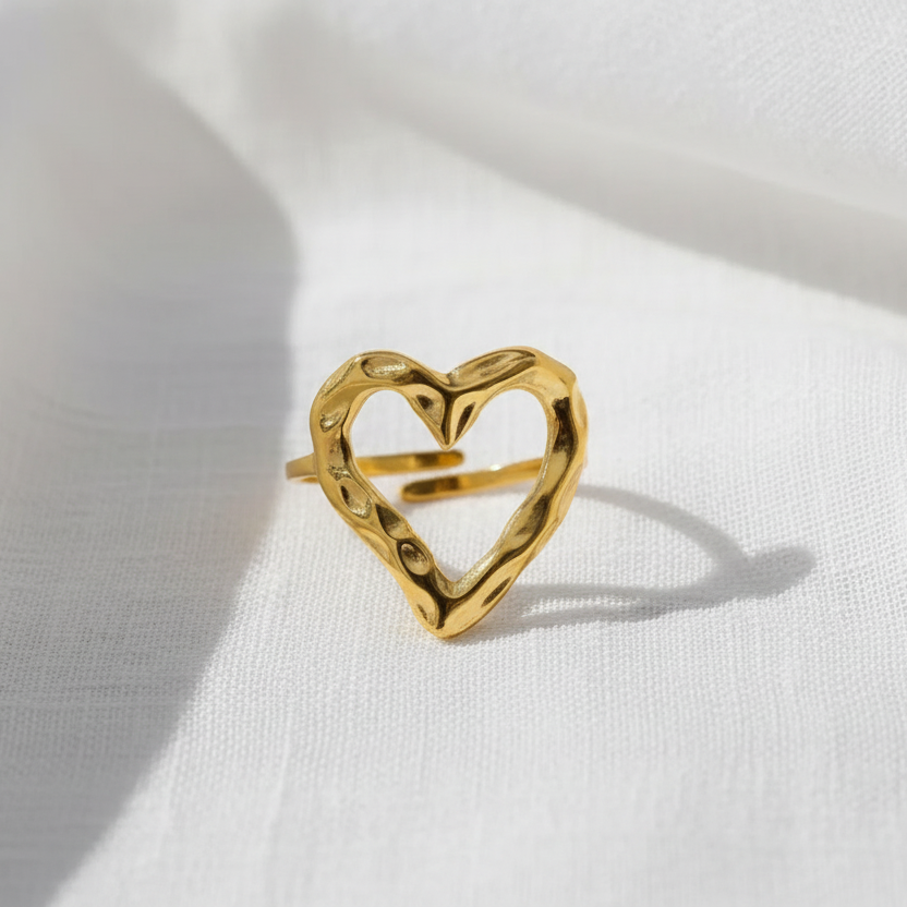 Gros plan sur une bague coeur stylisé ajouré et martelé en acier inoxydable doré.