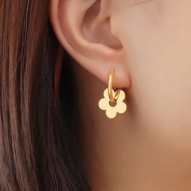 Femme portant des créoles en acier inoxydable doré avec fleur stylisée dorée, style bohème