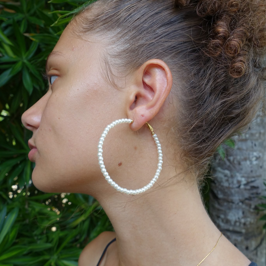 Créoles en acier 316L doré et véritables perles d'eau douce portées par une femme.