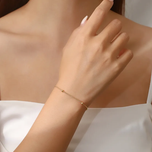 Femme portant un bracelet en acier inoxydable doré, fine maille serpent perlée, style bohème élégant