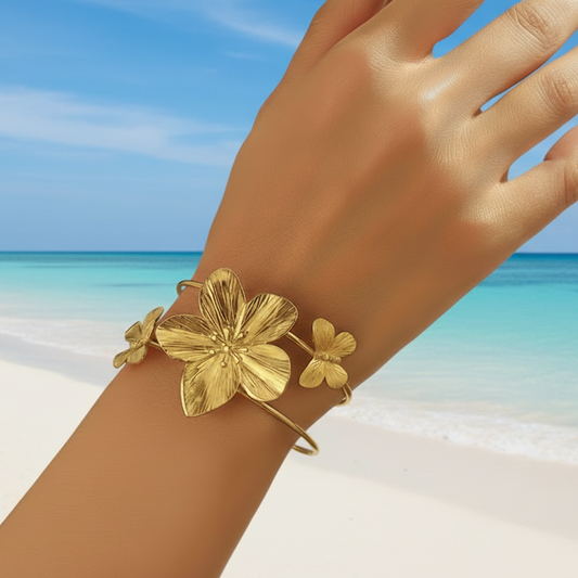 Femme portant un bracelet manchette en acier inoxydable doré, décoré d’une grande fleur tropicale et de deux papillons, style bohème
