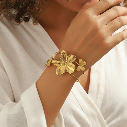 Bracelet manchette en acier inoxydable 316L doré, décoré d’une grande fleur tropicale et de deux papillons, porté sur un poignet.