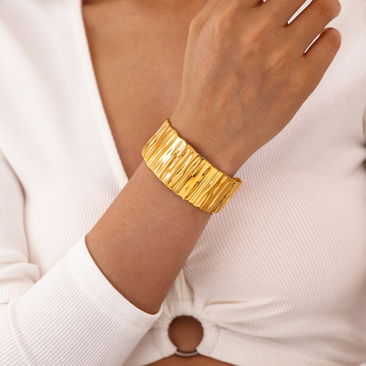 Femme portant un bracelet manchette large de 3 cm en acier inoxydable doré, finition martelée et brillante, bijou tendance au style chic et bohème