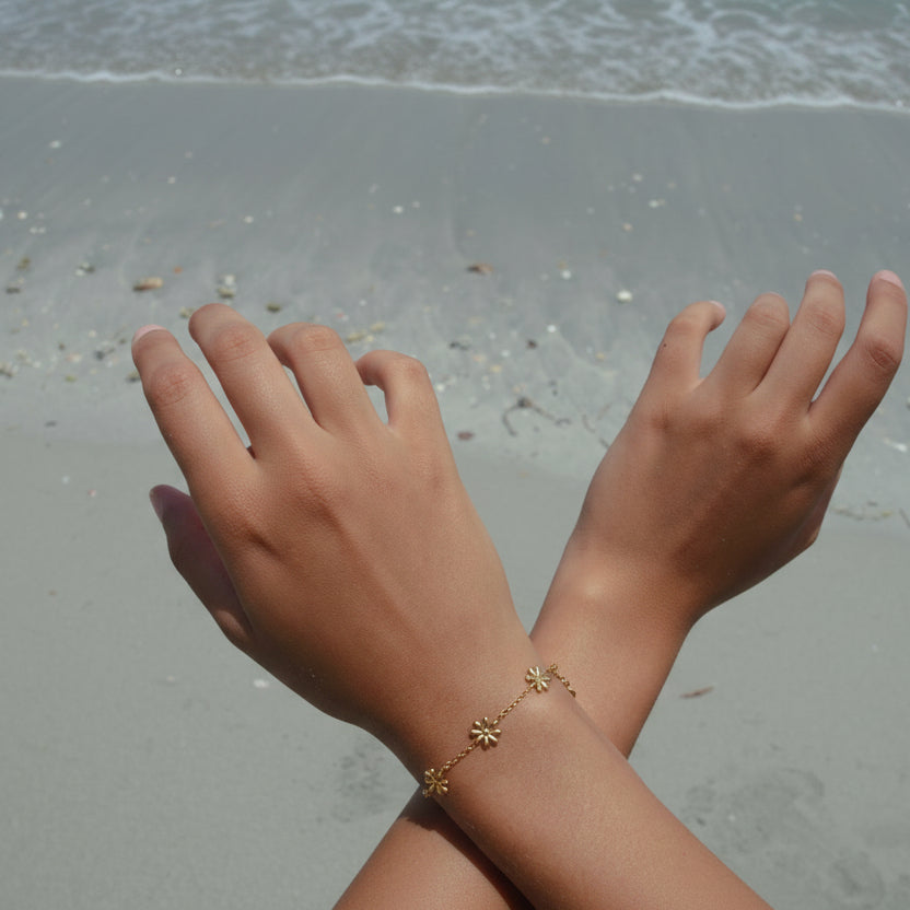Bracelet femme minimaliste en acier doré, chaîne fine et petites fleurs tendance porté à la plage