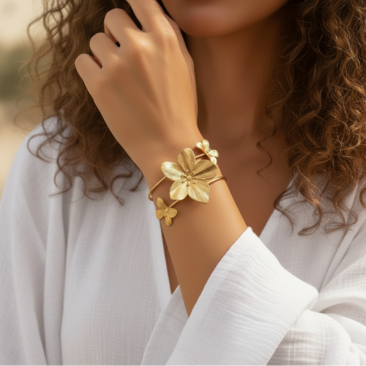 Bracelet manchette en acier inoxydable 316L doré, décoré d’une grande fleur tropicale et de deux papillons, porté sur un poignet.
