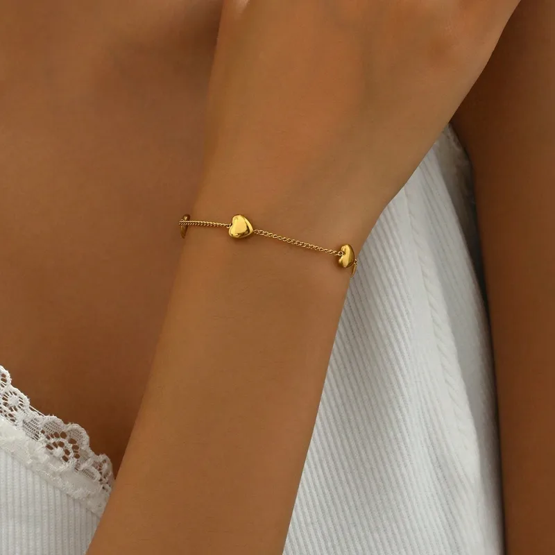 Femme portant un bracelet en acier inoxydable doré, maille gourmette fine ornée de 4 cœurs, style bohème élégant