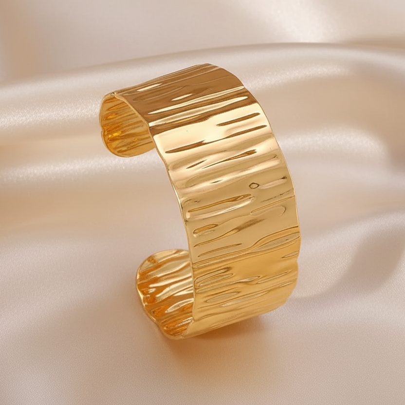 Gros plan sur un bracelet manchette large de 3 cm en acier inoxydable doré, finition martelée et brillante.