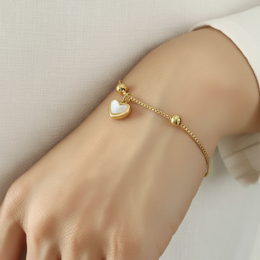 Bracelet fin en acier inoxydable 316L doré avec fermeture coulissante et pendentif cœur en nacre porté sur un poignet.