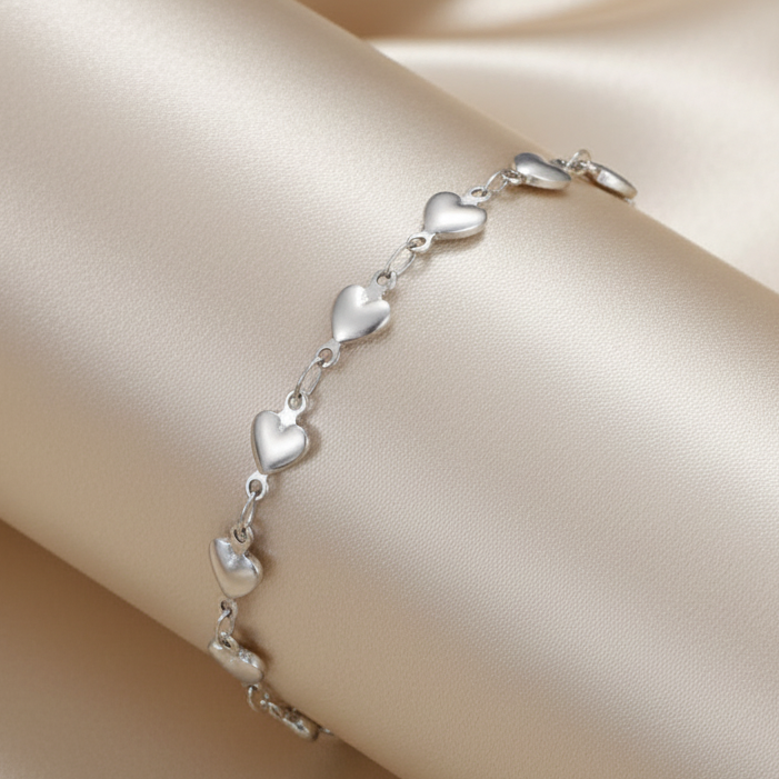Gros plan sur un bracelet de cheville argenté en acier inoxydable 316L à chaîne de petits coeurs.