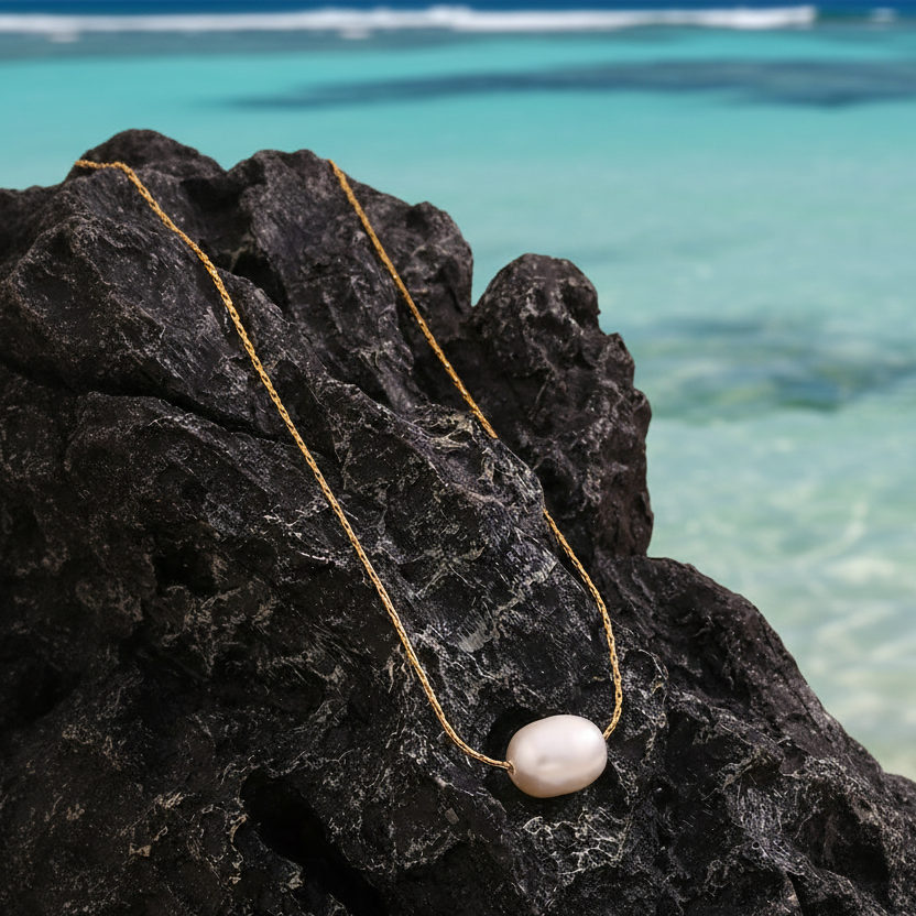 Collier en acier inoxydable 316L doré à chaîne ultra fine orné d'une perle d’eau douce blanche posé sur un rocher.