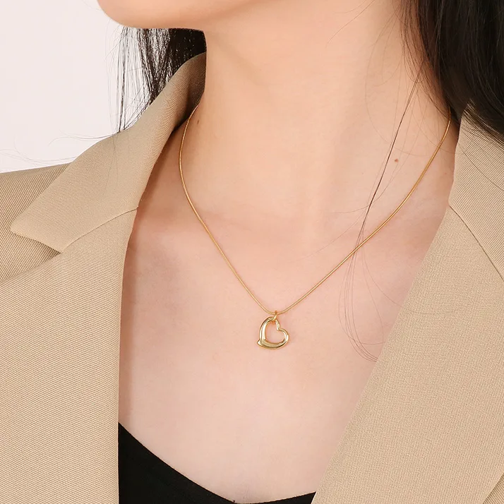 Femme portant un collier doré en acier inoxydable, maille serpent fine, pendentif cœur ajouré stylisé