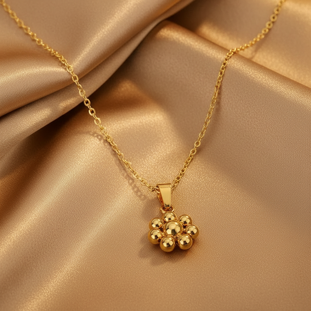 Gros plan sur un collier doré en acier inoxydable à fine chaîne maille forçat et pendentif fleur stylisée.