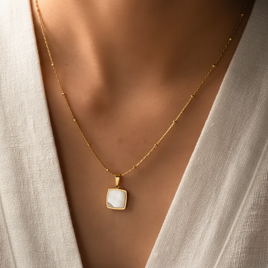 Femme portant un collier doré en acier inoxydable avec pendentif carré en nacre sur fine chaîne bambou et perles.