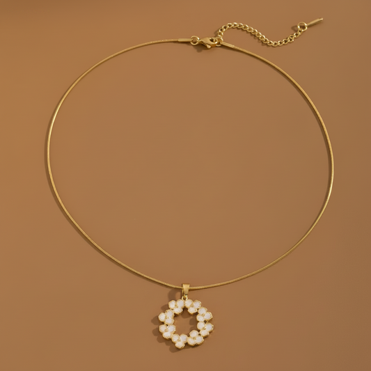 Collier en acier inoxydable doré à fine chaîne serpent orné d'un pendentif couronne de fleurs émaillé blanc.