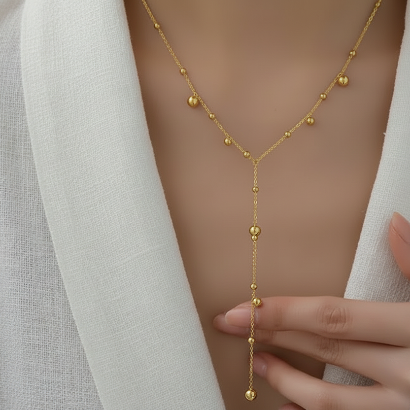 Femme portant un collier cravate doré en acier inoxydable à fine chaîne maille forçat et perles dorées, style bohème et tendance
