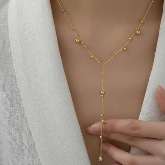 Femme portant un collier cravate doré en acier inoxydable à fine chaîne maille forçat et perles dorées.