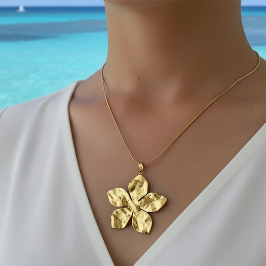 Femme portant un collier doré en acier inoxydable à chaîne maille serpent orné d'un pendentif grande fleur tropicale martelée.