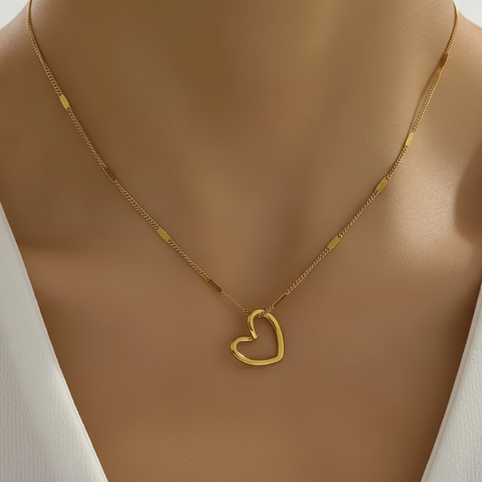 Femme portant un collier doré en acier inoxydable à chaîne maillons cubains fins alternés mailles plates et petit cœur ajouré, style intemporel