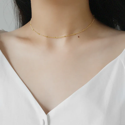 Femme portant un collier doré en acier inoxydable, maille gourmette et perles dorées