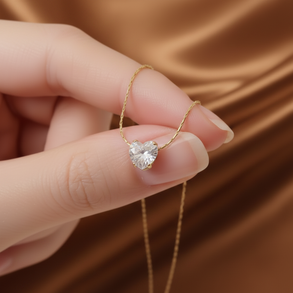 Gros plan sur un collier à chaîne ultra fine maille bambou en acier inoxydable 316L doré orné d'un pendentif petit coeur en zircon blanc.