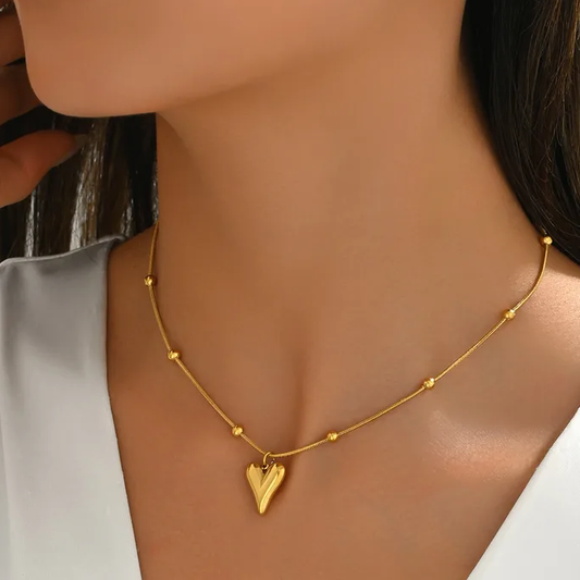 Femme portant un collier doré en acier inoxydable avec fine chaîne serpent perlée et pendentif coeur stylé