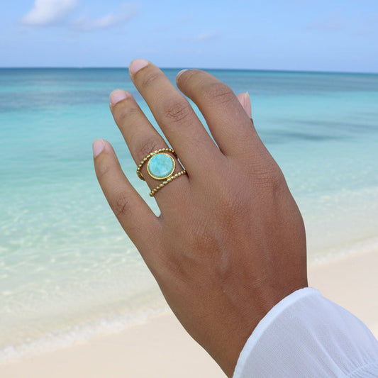 Main de femme portant une bague en acier inoxydable doré ornée d’une pierre naturelle amazonite.