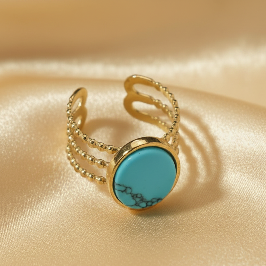 Gros plan sur une bague dorée en acier inoxydable ornée d'une pierre naturelle turquoise.