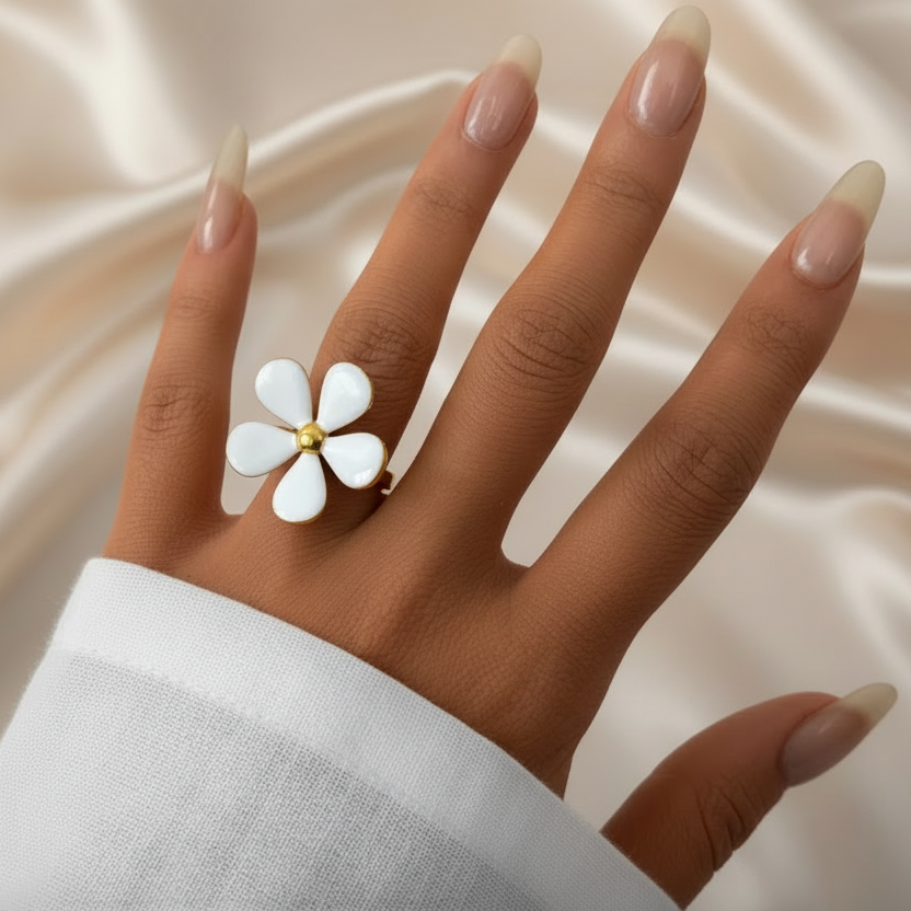 Main de femme portant une bague fleur en acier doré et émail blanc.