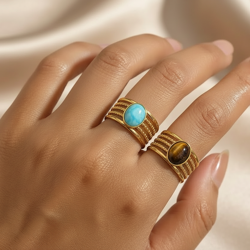 Bagues dorées en acier inoxydable et pierre naturelle turquoise et oeil de tigre portée sur une main de femme.