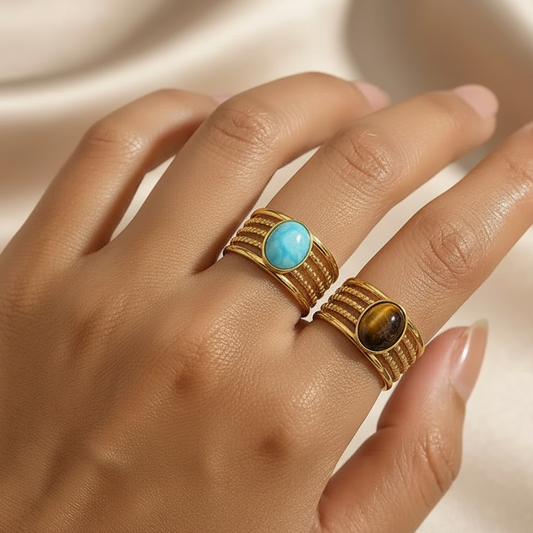 Bagues dorées en acier inoxydable et pierre naturelle turquoise et oeil de tigre portée sur une main de femme.