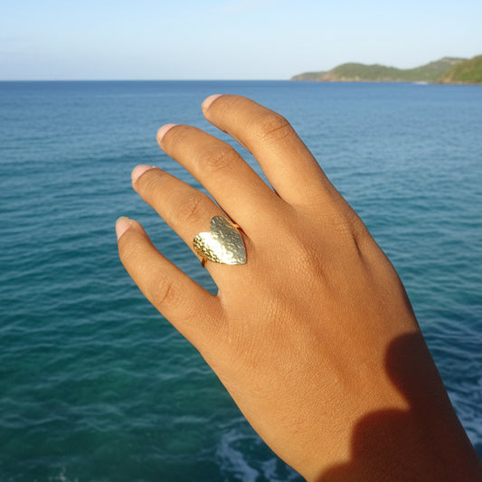 Main de femme portant une bague coeur stylisé et martelé en acier inoxydable doré.