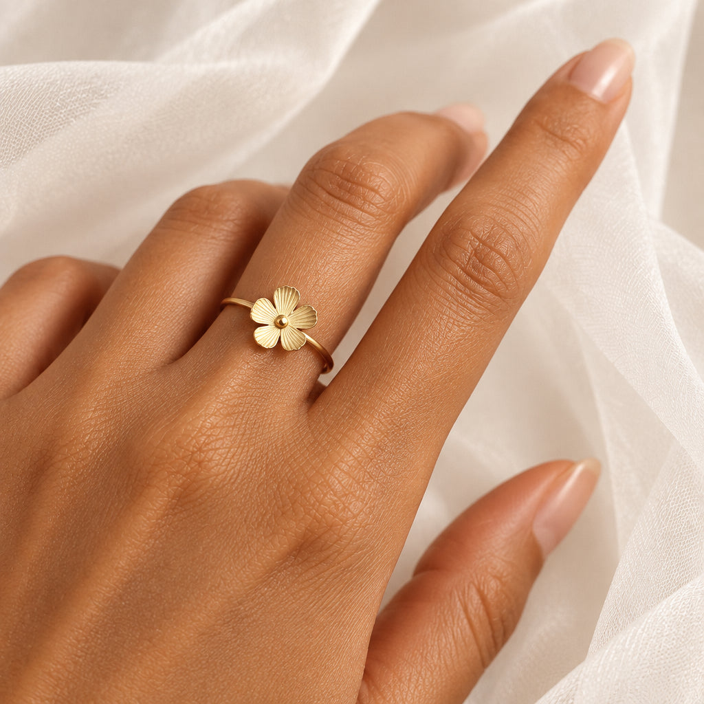 Gros plan sur une bague petite fleur stylisée ajustable en acier inoxydable doré portée sur une main de femme.