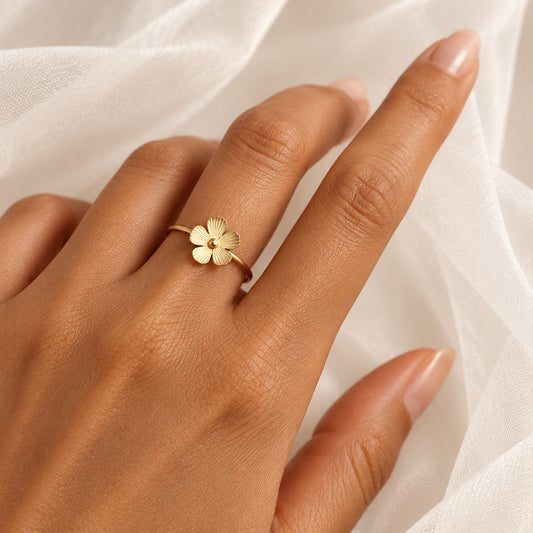 Gros plan sur une bague petite fleur stylisée ajustable en acier inoxydable doré portée sur une main de femme.