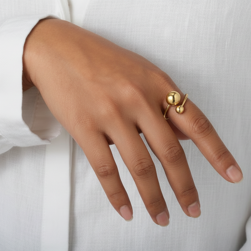 Main de femme portant une bague en acier inoxydable doré ornée d'une grande et petite perle en acier.