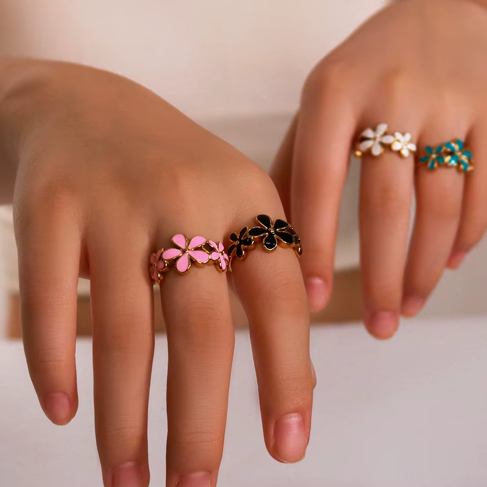Bague dorée ajustable en acier inoxydable avec trois fleurs en émail, portée sur la main d’une femme, bijou bohème, disponible en bleu, rose, noir et blanc