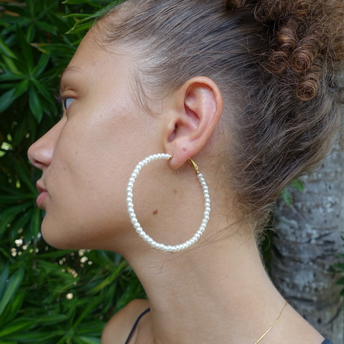 Créoles en acier 316L doré et véritables perles d'eau douce portées par une femme.