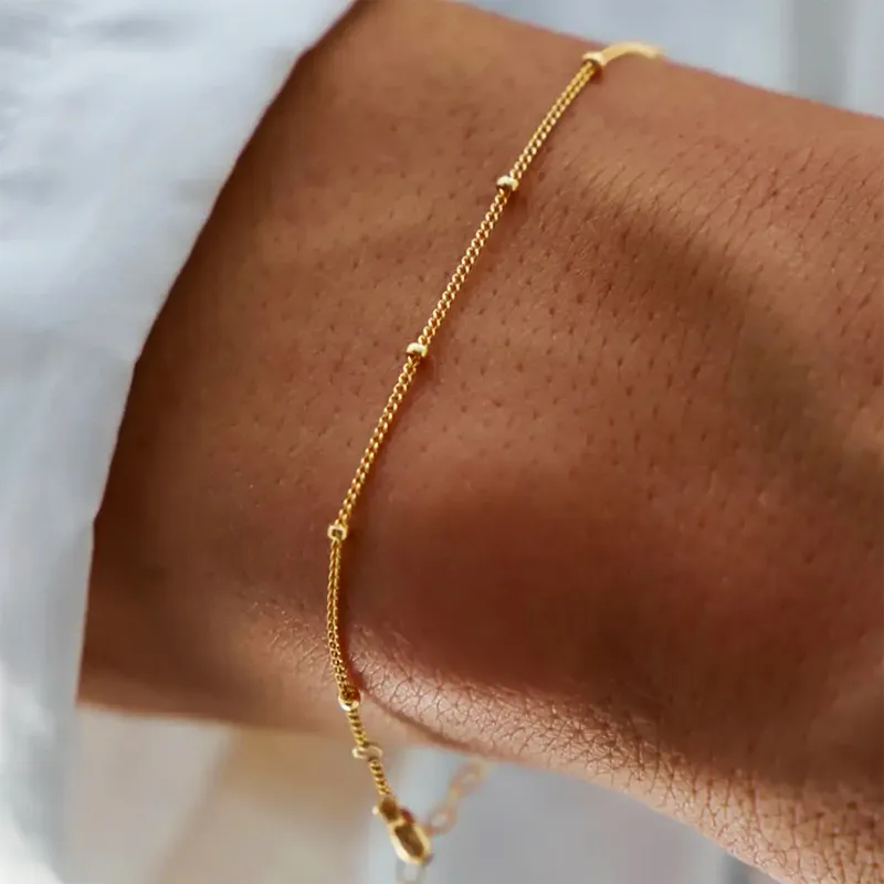 Femme portant un bracelet maille gourmette fine avec perles dorées en acier inoxydable 316L, bijou tendance chic et minimaliste 