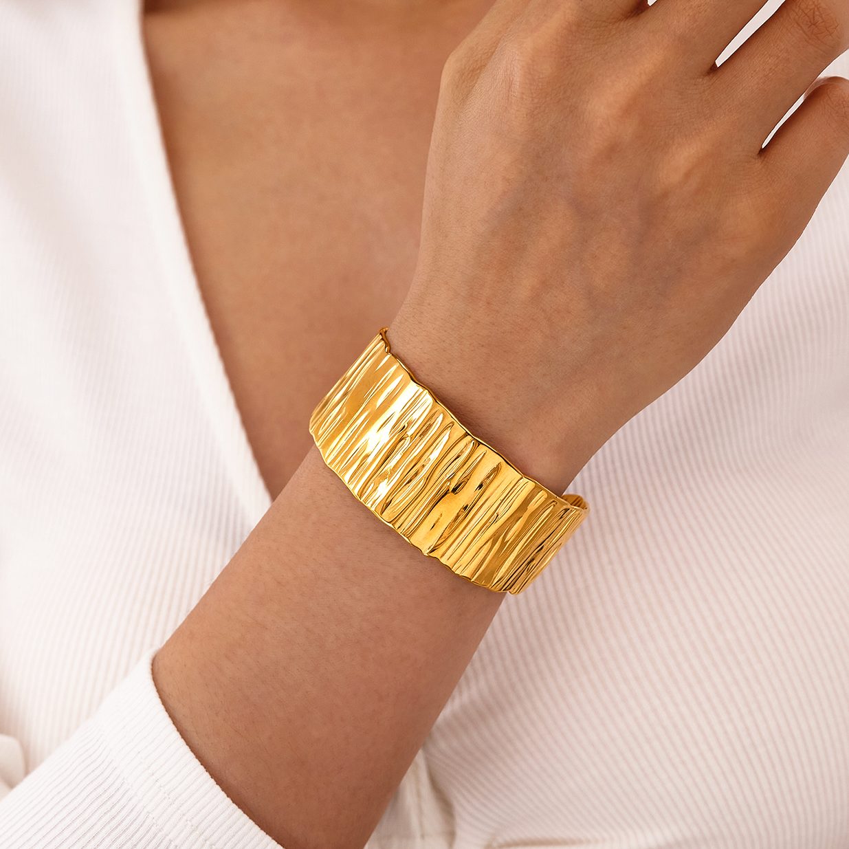 Bracelet manchette large de 3 cm en acier inoxydable doré, finition martelée et brillante, porté sur un poignet.